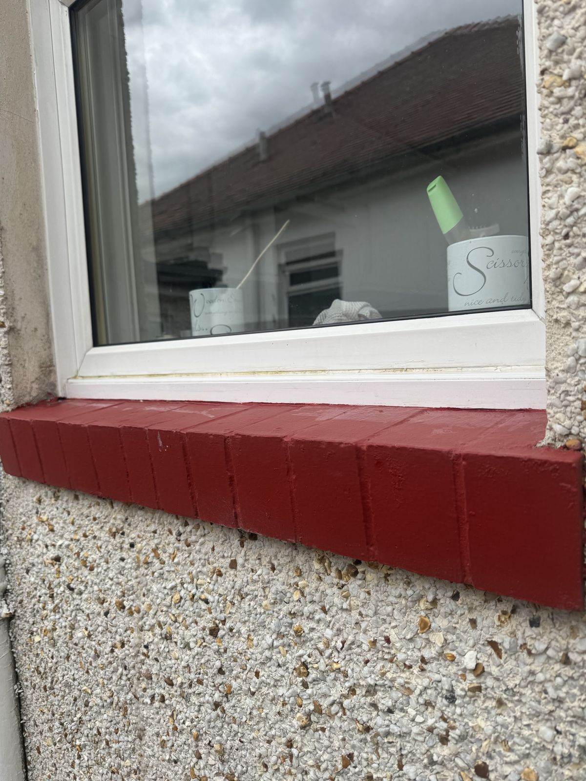A white window above a red sill on a pebble-dashed wall