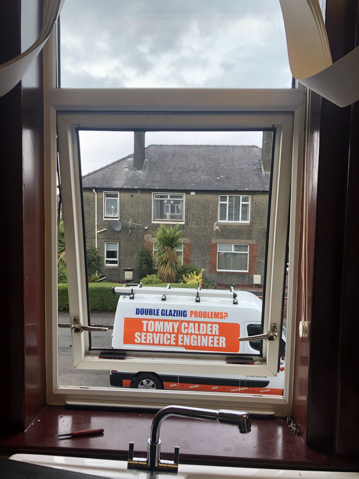 Tommy Calder's signwritten van, 'Double glazing problems? Tommy Calder Service Engineer', seen through an open window